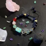 Cancer birthstone bracelet surrounded by raw pink and white crystals on a dark surface.