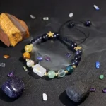 Gemini birthstone bracelet resting on a dark surface next to raw yellow and clear crystals.