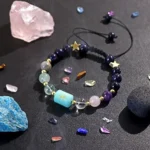 Pisces birthstone bracelet resting near raw amethyst and clear quartz clusters on a dark surface.