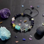 Scorpio birthstone bracelet resting near raw obsidian and malachite specimens on a dark surface.