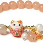 Peach-colored beaded bracelet with a decorative Maneki-Neko charm and gold accents.